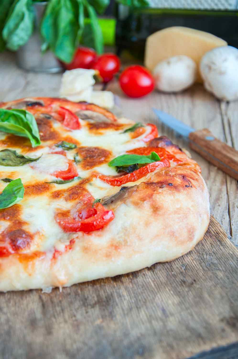 Pizza mit dickem Rand, Tomaten und frischem Basilikum