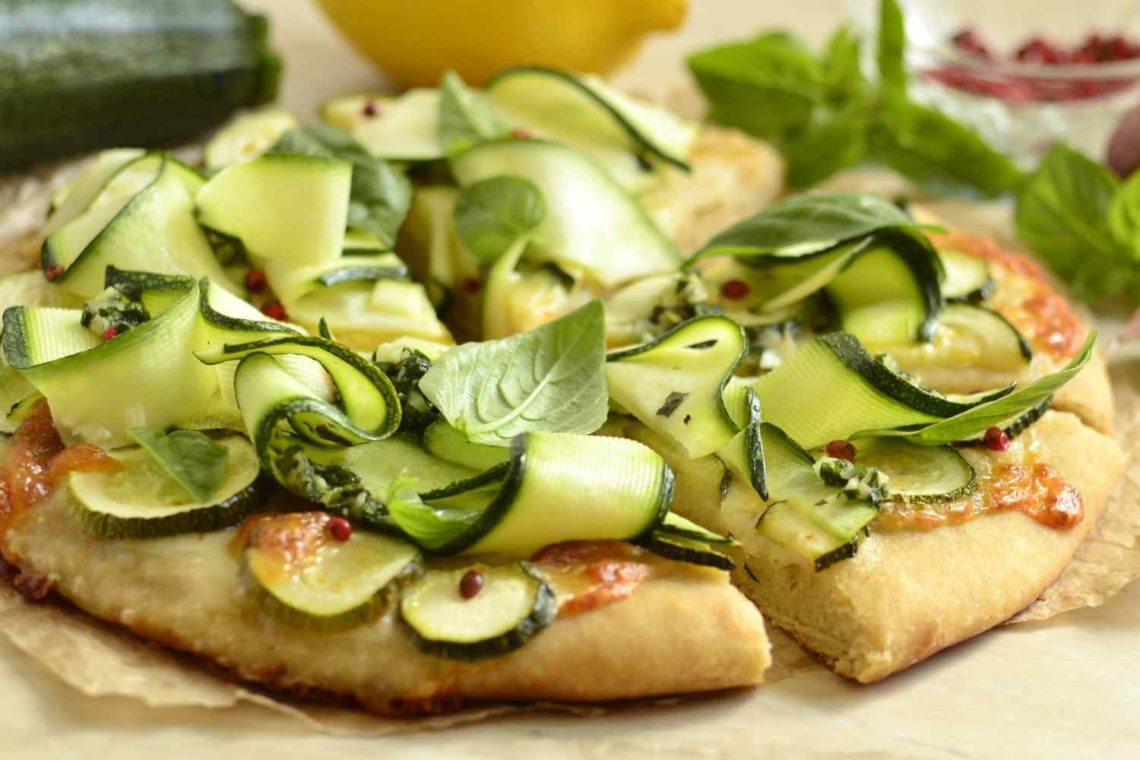 Krosse Quinoapizza belegt mit Zucchinistreifen, Gurkenscheiben und Basilikum