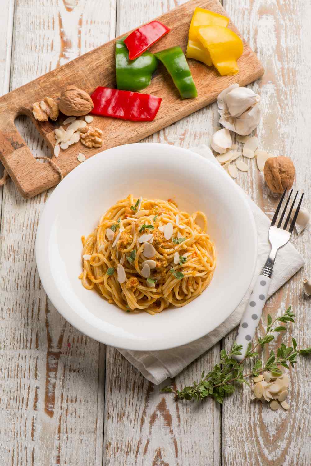 Spaghetti mit pesto auf Teller, Geschnittene Paprika und Nüsse im Hintergrund