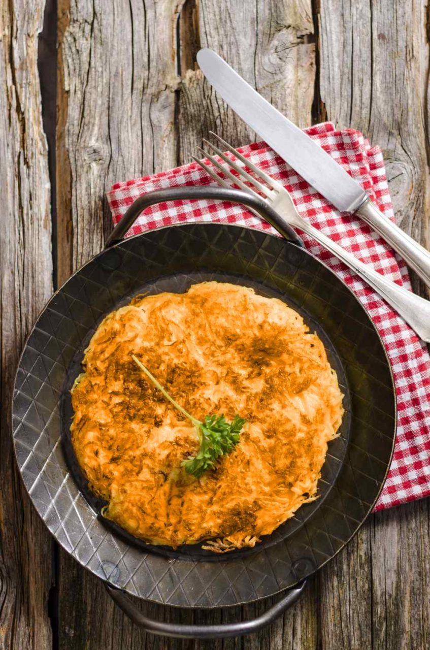 Pfanne auf grobem Holztisch mit einem goldbraunen Süßkartoffelrösti